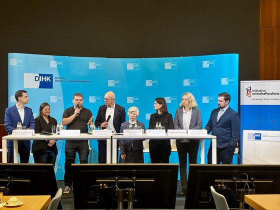 Insgesamt acht Männer und Frauen stehen auf der Bühne und unterhalten sich. Im Hintergrund ein blauen Banner des DIHK.